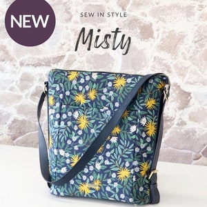 May include: A navy blue convertible backpack bag with a floral pattern of yellow and white flowers and green leaves. The bag has a dark blue strap and gold-colored hardware. The text "NEW" and "Misty" are visible.