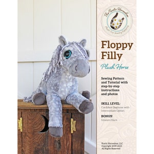 May include: A soft, grey plush horse with large blue eyes and a white mane, sitting on a wooden box. The text on the right reads "Floppy Filly Plush Horse" and details about the sewing pattern and skill level.