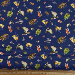 May include: A dark blue fabric featuring a repeating pattern of colorful fishing flies and green leaves. The fishing lures are depicted in shades of yellow, orange, brown, and white, scattered across the navy background in a dense, uniform arrangement.