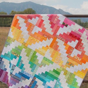 May include: A quilt featuring a vibrant rainbow log cabin pattern with various colorful fabric prints and white segments. The top banner reads Mapleton Avenue A Quilt Pattern by Sassafras Lane Designs and the bottom banner reads SASSLN #0061.