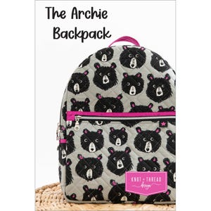 May include: A grey quilted backpack featuring a pattern of black bear faces. The backpack has a pink zip and handle. The text "The Archie Backpack" is at the top. The brand name is "Knot + Thread design".