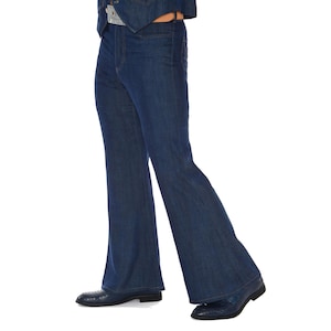 May include: Dark blue denim bell-bottom jeans. The jeans have a high waist and a flared leg from the knee down. The person is wearing dark blue shoes. The jeans are part of a denim outfit.