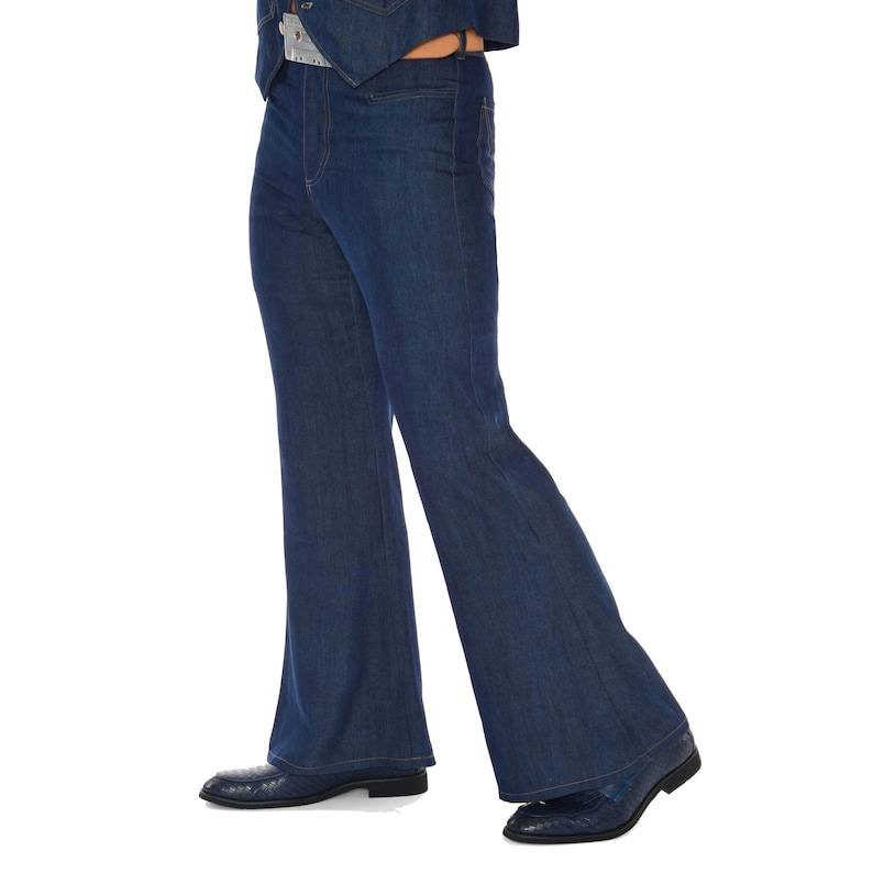 May include: Dark blue denim bell-bottom jeans. The jeans have a high waist and a flared leg from the knee down. The person is wearing dark blue shoes. The jeans are part of a denim outfit.