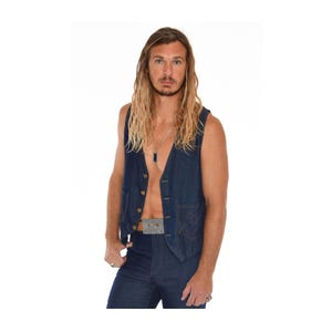 May include: A dark blue denim vest with a V-neck and button closure. The vest has two front pockets and is paired with matching denim pants. A silver necklace and belt with a cassette tape design complete the look.