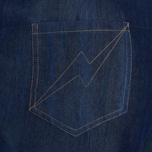 May include: Close-up of a dark blue denim pocket with a lightning bolt design stitched in a light tan thread. The pocket is rectangular with a curved bottom and is sewn onto the denim fabric with matching thread.