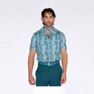 May include: A light blue short-sleeved button-down shirt with a pattern of repeated images of women. The shirt has a teal blue collar and a teal blue belt.