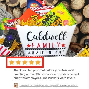 Puede incluir: Un cubo de palomitas blanco con el texto "Caldwell Family Movie Night" impreso en &eacute;l. El cubo est&aacute; lleno de varios bocadillos, incluyendo dulces, palomitas de ma&iacute;z y un control remoto.