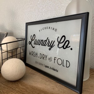 May include: Black and white sign with the text "PICKERING Laundry Co. WASH, DRY AND FOLD SELF-SERVE | open 24 hours" on a white background.