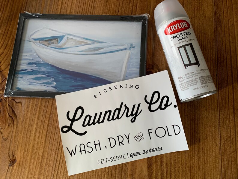 May include: A white sign with black text that reads "PICKERING Laundry Co. WASH, DRY AND FOLD SELF-SERVE I open 24 hours". A can of Krylon Frosted Glass spray paint is in the background.
