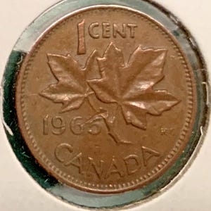 Può includere: Una moneta canadese da un centesimo color rame con due foglie d'acero al centro. Il testo 1 CENT è stampato sopra le foglie, con l'anno 1965 e la parola CANADA incisi sotto le foglie in una disposizione circolare.