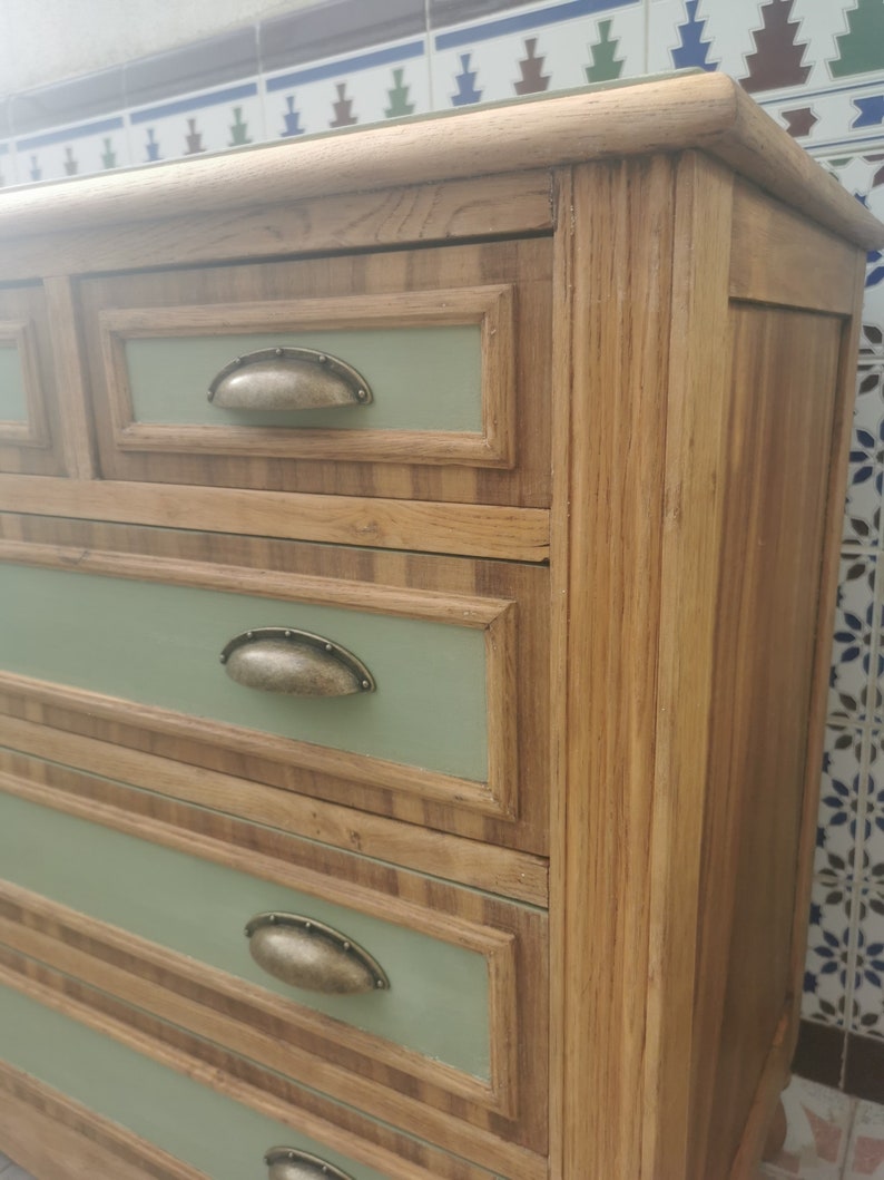 May include: A wooden dresser with four drawers. The drawers have a light green painted front with a dark wood trim. Each drawer has a metal knob.