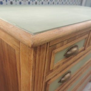 May include: A wooden dresser with five drawers. The drawers have a light green painted finish and brass handles. The top of the dresser is a light green painted surface.