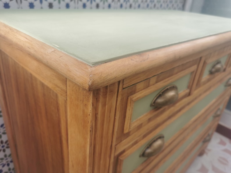 May include: A wooden dresser with five drawers. The drawers have a light green painted finish and brass handles. The top of the dresser is a light green painted surface.