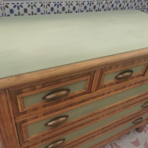 May include: A light green dresser with five drawers. The drawers have a wood grain pattern and brass handles. The top of the dresser is painted a light green color.