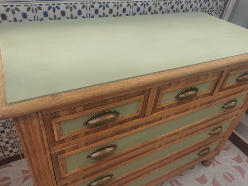 May include: A light green dresser with five drawers. The drawers have a wood grain pattern and brass handles. The top of the dresser is painted a light green color.