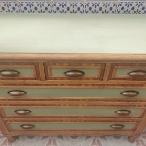 May include: A five-drawer dresser with a light green top and wooden drawers. The drawers have a light brown wood veneer with a woven pattern and brass oval-shaped handles.