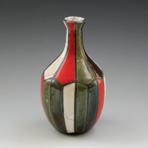 May include: A decorative ceramic vase with a narrow neck and a rounded body. The vase is segmented with vertical panels of red, white, green, and brown. The vase is approximately 8 inches tall.