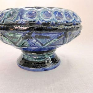 May include: A blue and green ceramic bowl with a pedestal base. The bowl has a textured surface with a geometric pattern.