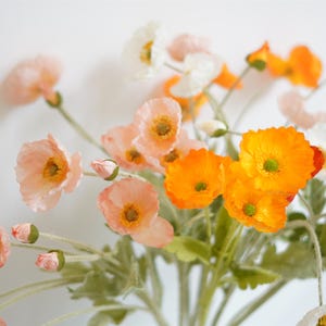 Puede incluir: Un ramo de flores artificiales con flores de amapola de color melocotón, naranja y blanco. Las flores tienen tallos y hojas verdes.