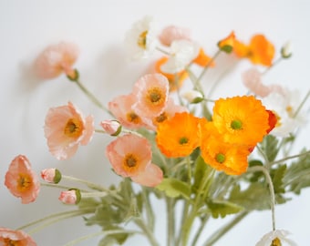 Puede incluir: Un ramo de flores artificiales con flores de amapola de color melocotón, naranja y blanco. Las flores tienen tallos y hojas verdes.