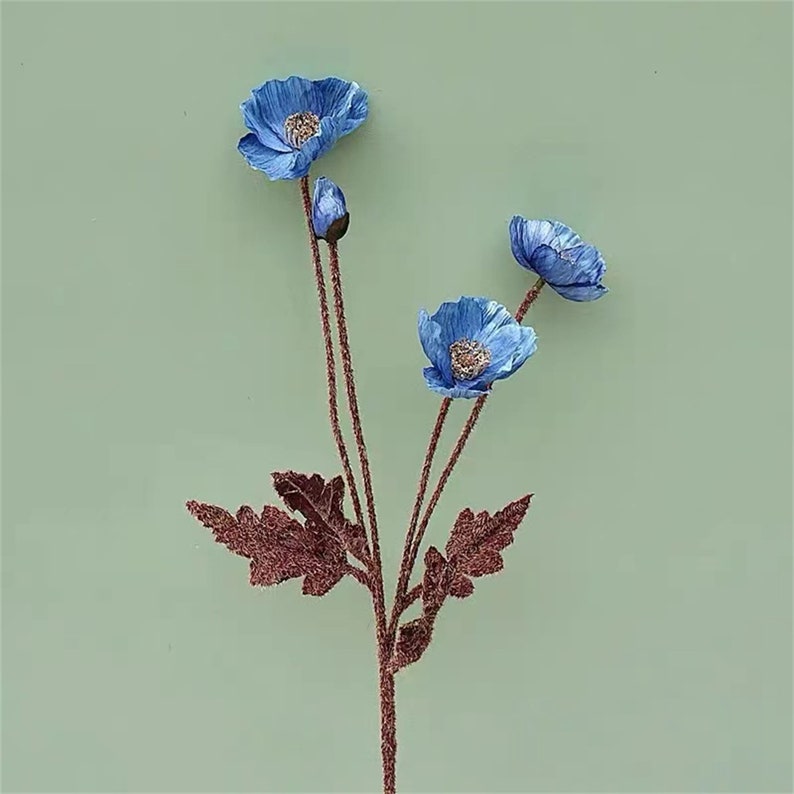 Puede incluir: Un ramo de tres flores de amapola artificiales azules con tallos y hojas marrones.