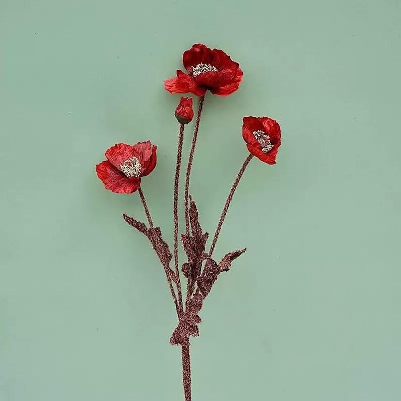 Puede incluir: Un ramo de tres flores de amapola rojas con detalles de purpurina. Los tallos son marrones y tienen peque&ntilde;as hojas verdes.