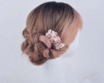 May include: A pink and white floral hair comb with a delicate design. The comb is made of metal and has a cluster of small flowers.