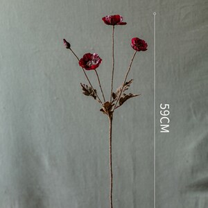 Puede incluir: Un ramo de tres flores de amapola rojas artificiales con tallos y hojas marrones. Las flores miden 59 cm de alto.
