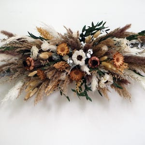 Pode incluir: Um arranjo floral seco com capim-dos-pampas branco, marrom e bege, flores secas e folhagem. O arranjo é perfeito para um casamento, uma festa ou a decoração da casa.