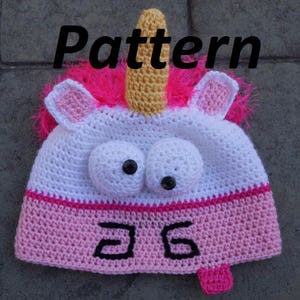 May include: A white crocheted unicorn hat with pink and yellow accents. The hat has large googly eyes and a pink and white striped brim. The hat has the number "36" embroidered on the brim.