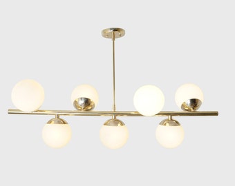 May include: A gold-toned chandelier with six white globe-shaped light fixtures. The chandelier has a long, straight bar with the light fixtures attached to it.