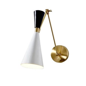 May include: A gold-toned wall sconce with a white and black cone-shaped shade. The sconce has a flexible arm that can be adjusted to direct the light.