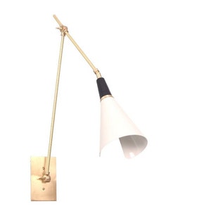 May include: A brass wall sconce with a white and black cone-shaped shade. The sconce has a long, adjustable arm.
