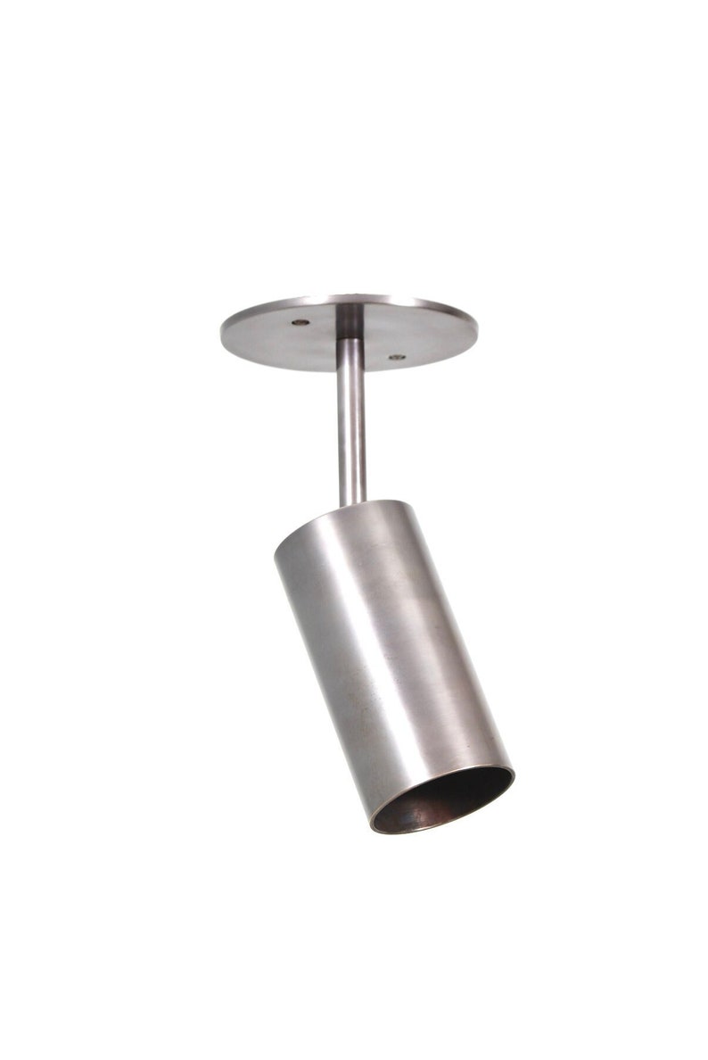 May include: A silver ceiling light fixture with a cylindrical shade that is angled downwards. The fixture has a round base with two screws.