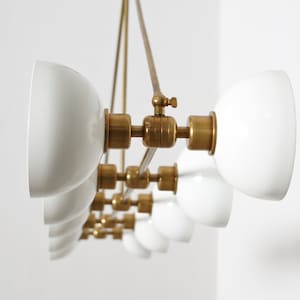 May include: A brass and white glass chandelier with multiple lights. The chandelier has a modern design with a sleek, minimalist aesthetic.