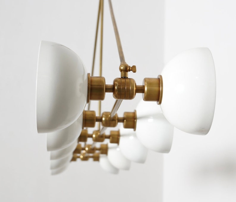 May include: A brass and white glass chandelier with multiple lights. The chandelier has a modern design with a sleek, minimalist aesthetic.