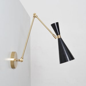 May include: A brass wall-mounted light fixture with a black cone-shaped shade. The arm of the light fixture is adjustable and can be moved to different positions.