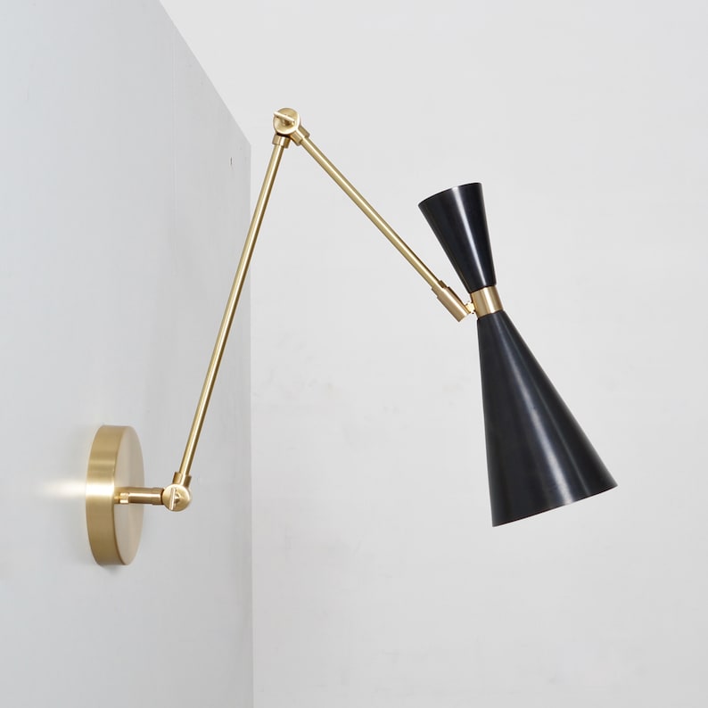 May include: A brass wall-mounted light fixture with a black cone-shaped shade. The arm of the light fixture is adjustable and can be moved to different positions.