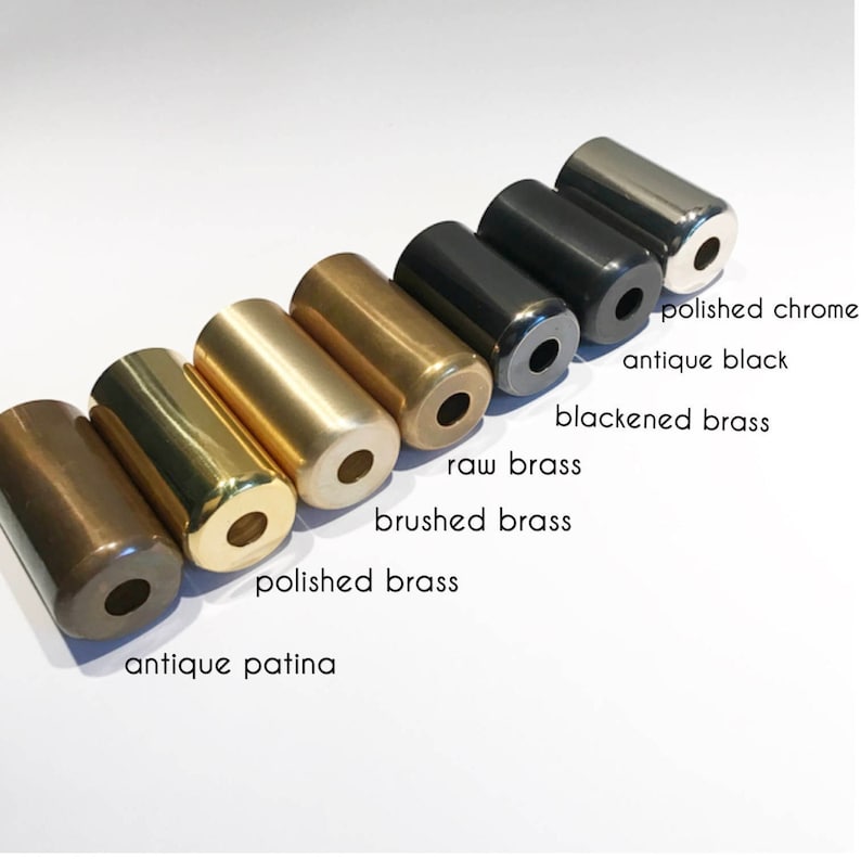 Puede incluir: Primer plano de ocho tapas de cilindro de metal en diferentes acabados: p&aacute;tina antigua, lat&oacute;n pulido, lat&oacute;n cepillado, lat&oacute;n en bruto, lat&oacute;n ennegrecido, negro antiguo y cromo pulido.