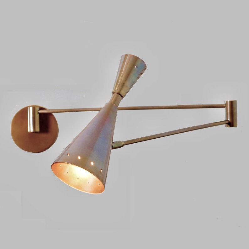 Puede incluir: Una l&aacute;mpara de pared de lat&oacute;n con dos pantallas c&oacute;nicas ajustables. Las pantallas est&aacute;n inclinadas en direcciones opuestas y tienen un acabado met&aacute;lico c&aacute;lido.