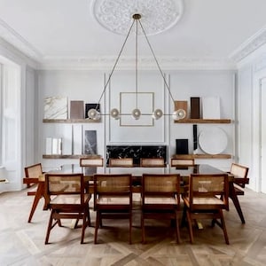 May include: A dining room with a long wooden table and eight chairs. The table is set with a black tablecloth and a brass chandelier hangs above. The walls are white and the floor is a dark wood.