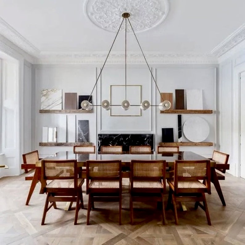 May include: A dining room with a long wooden table and eight chairs. The table is set with a black tablecloth and a brass chandelier hangs above. The walls are white and the floor is a dark wood.