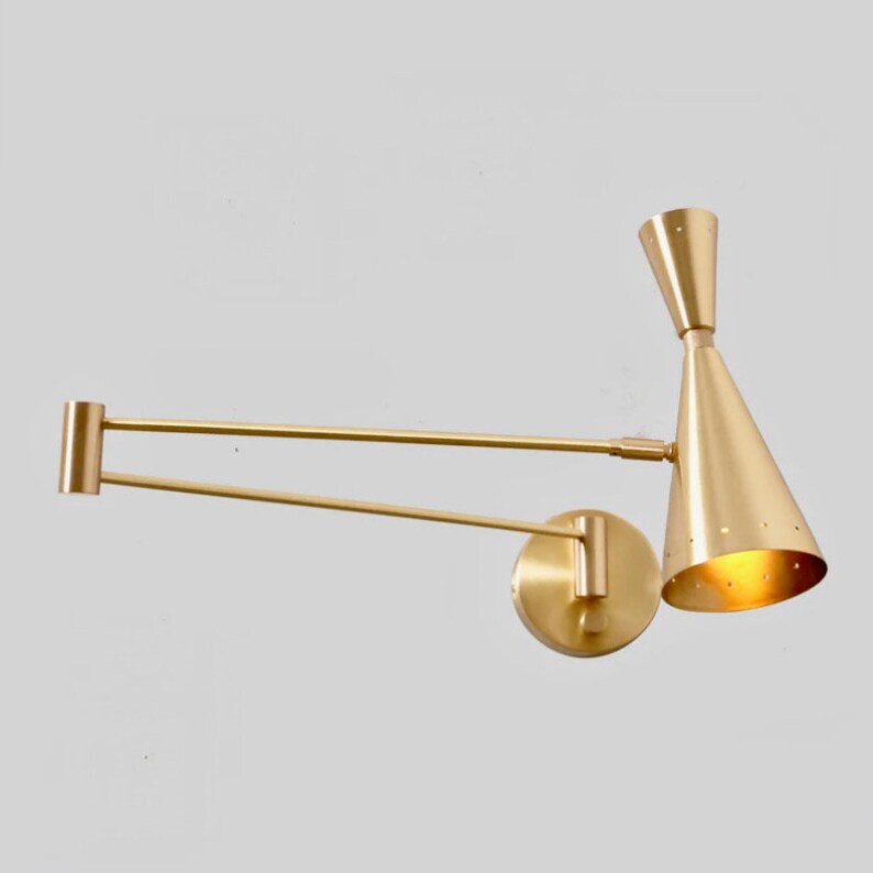 Puede incluir: Una l&aacute;mpara de pared dorada con un brazo largo y ajustable y una pantalla en forma de cono. La pantalla tiene un patr&oacute;n de peque&ntilde;os agujeros.