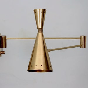 Puede incluir: Una l&aacute;mpara de pared de lat&oacute;n con una pantalla en forma de cono y un brazo giratorio. La l&aacute;mpara tiene un dise&ntilde;o minimalista y es perfecta para interiores modernos o contempor&aacute;neos.