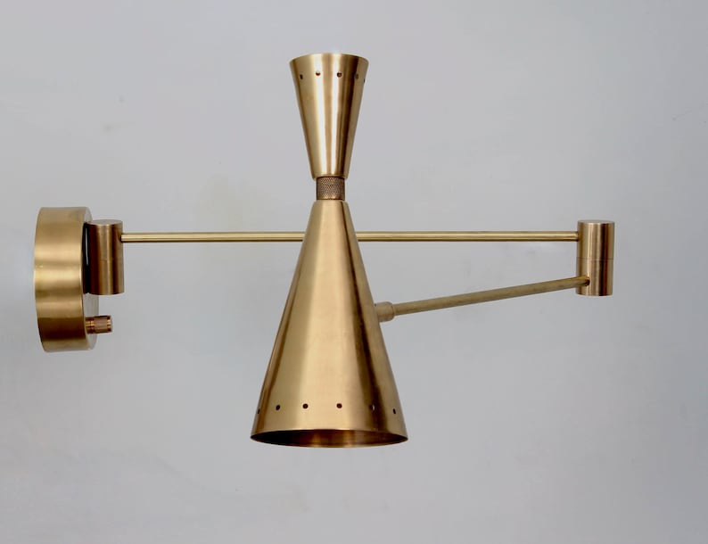 Puede incluir: Una l&aacute;mpara de pared de lat&oacute;n con una pantalla en forma de cono y un brazo giratorio. La l&aacute;mpara tiene un dise&ntilde;o minimalista y es perfecta para interiores modernos o contempor&aacute;neos.