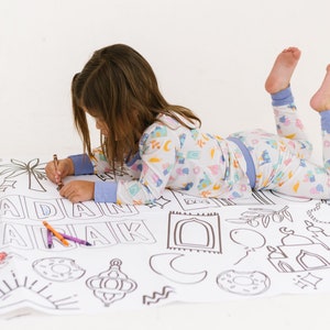 May include: A child in pajamas is coloring a large sheet of paper with black and white illustrations of Islamic symbols and the words "Ramadan Mubarak".