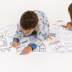 May include: Two children in pajamas color a large white sheet with black outlines of Islamic symbols and the words "Eid Mubarak".
