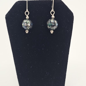 May include: A pair of dangle earrings with iridescent, mosaic-like beads. The beads are spherical, with a mix of blues, greens, and silver. The earrings have silver-colored hooks and small silver beads at the bottom of the sphere.