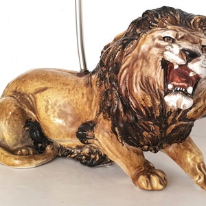 May include: A ceramic lion ornament in a roaring pose. The lion has a tan body, a brown mane, and a red mouth. The figurine is detailed and appears to be a decorative item.