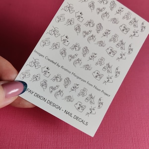 Può includere: Un foglio di adesivi per unghie bianchi con disegni a linea nera di due volti in varie pose. Il testo "Images Created by Kristina Margaryan from Noun Project" e "FAY DIXON DESIGN - NAIL DECALS" è stampato sul foglio.